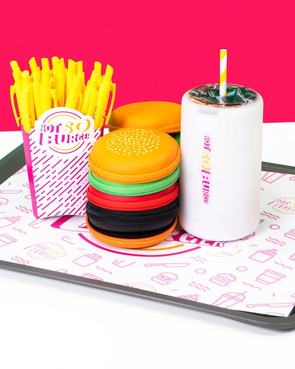 A tray of burger-themed promotional items: yellow pens in a fry box, stacked burger zip pouches and a white drink tumbler with a straw, on a pink and white background